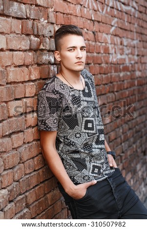 Young hipster guy in a black shirt standing near red brick wall with graffiti.