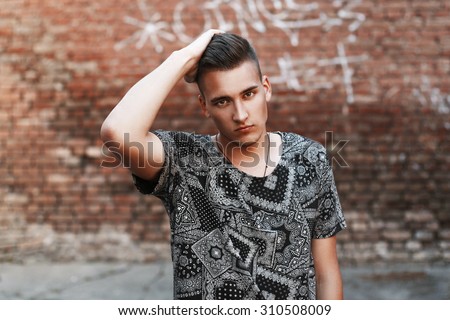 Close-up portrait of a young hipster in a black vintage t-shirt on a background of red bricks.