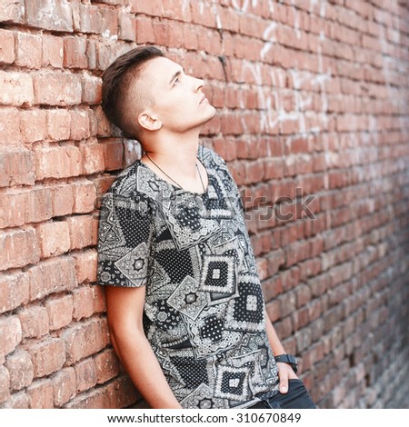 Young hipster standing near red brick wall. Vintage textile shirt
