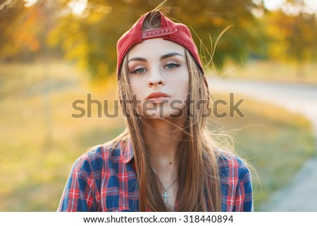 Autumn portrait of a beautiful girl in a baseball cap and a shirt at sunset.