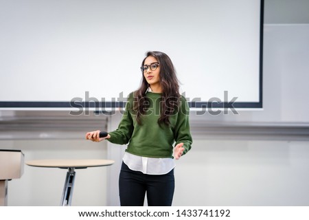 Portrait of a young, beautiful, attractive and intelligent-looking Indian Asian woman wearing spectacles in a sweater giving a business presentation to an audience. 