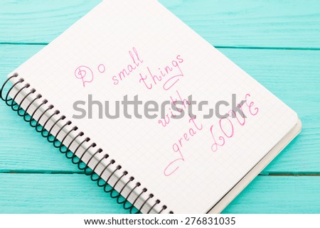 Phrase in notebook - do small things with great love on blue wooden background. Top view. Selective focus. Macro
