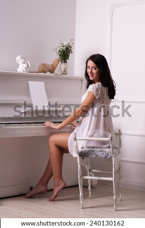 The beautiful girl  sits on a chair about the white piano