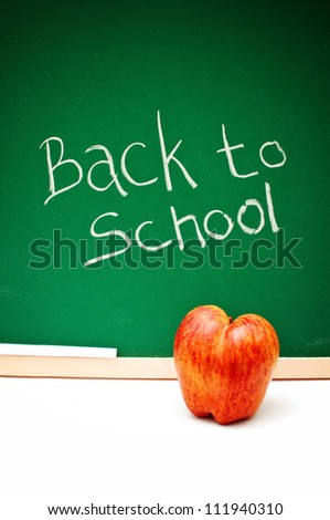 Back to school note written with white chalk on a green chalkboard, a red apple  in front of the board.