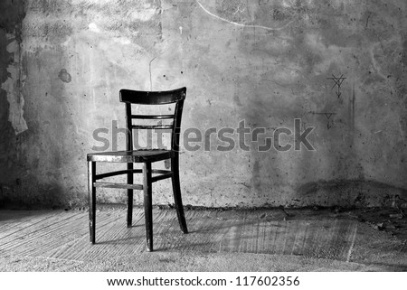 Vintage old black wooden chair in grungy interior. Loneliness, estrangement, alienation concept.