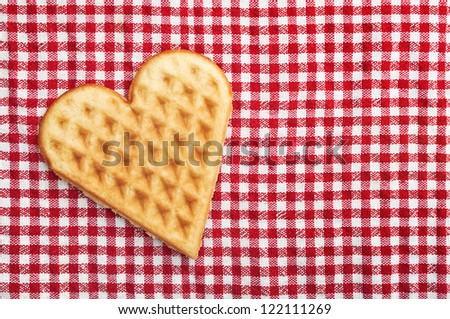 Heart shaped waffle cookie on checkered table cloth, top view