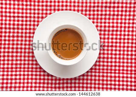 Coffee cup on table. Cup of domestic black coffee ob red and white checkered table cloth background, top view