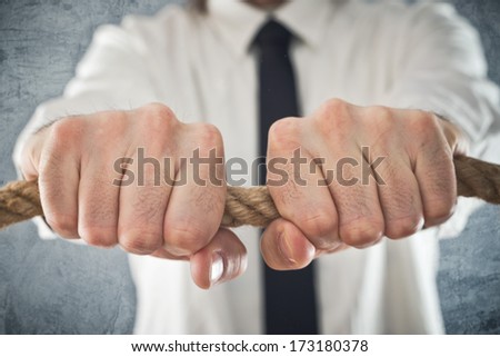 Businessman holding tight to a rope. Concept of business problems, difficult business situation.