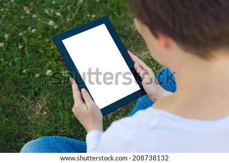 Woman holding digital tablet computer with blank white screen and browsing the internet while sitting on green grass in the park.