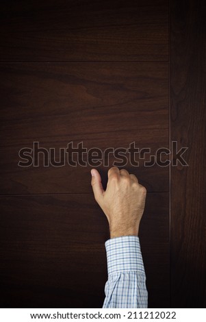 Male hand is knocking on wooden door, conceptual image. Visitor or guest is at the door.