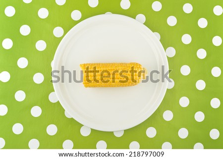 Cooked Corn maize cob half on a flat plate served as a dieting dinner above polka dots table cloth, top view