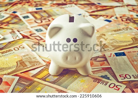 Piggy Coin Bank standing on fifty Euro banknotes pile as home budget theme illustrative image.