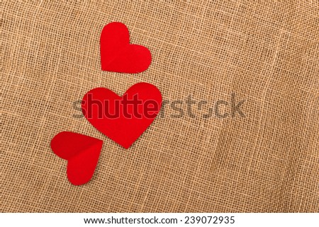 Valentine\'s Day background with red paper hearts on natural jute burlap texture as copy space.