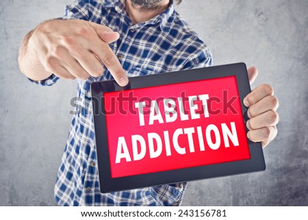 Casual man pointing to 10 inch display of digital tablet with Tablet Addiction displayed on the screen.