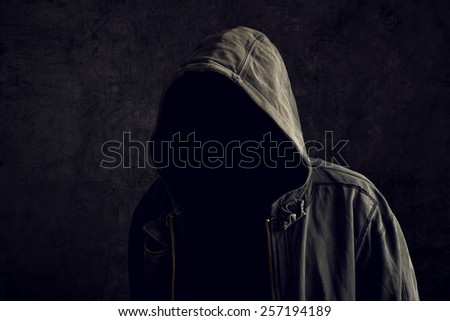 Faceless unknown and unrecognizable man without identity wearing hood in dark room, spooky criminal person.