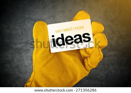 Male Hand in Yellow Leather Construction Working Protective Gloves Holding Horizontal Business Card with We Need More Ideas Demand.
