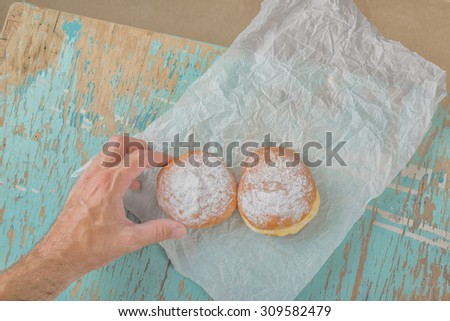 Male hand reaches and taking sweet sugary donut from rustic wooden kitchen table, tasty bakery doughnuts overhead shot, top view