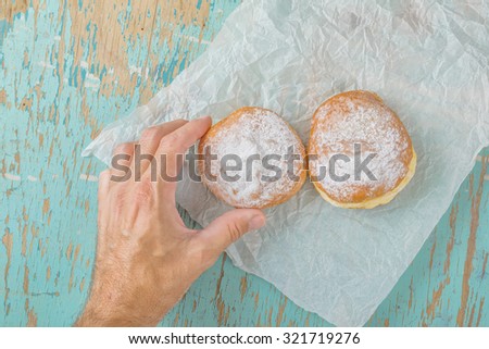 Male hand reaches and picking sweet sugary donut from rustic wooden kitchen table, tasty bakery doughnuts overhead shot, top view