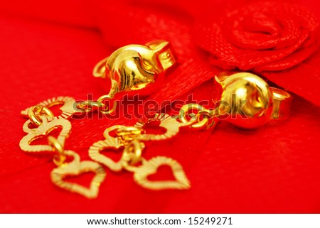 A pair of earrings beside the red rose ribbon.