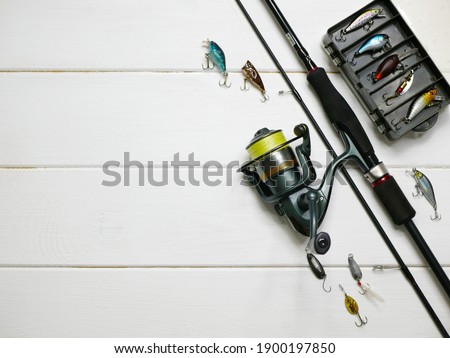 Fishing tackles lay on white wooden boards. Set of fishing tackles. Top view on spool, rod, spoons, wobblers and lure box.