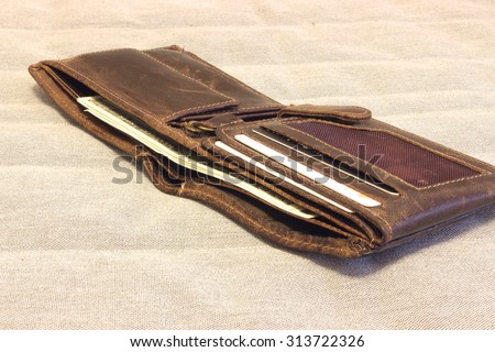Brown natural leather wallet  on a folded hessian cloth. Wallet filled up with money and plastic cards.