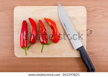 Red hot chili pepper and knife sits on a wood chopping board on wooden background.