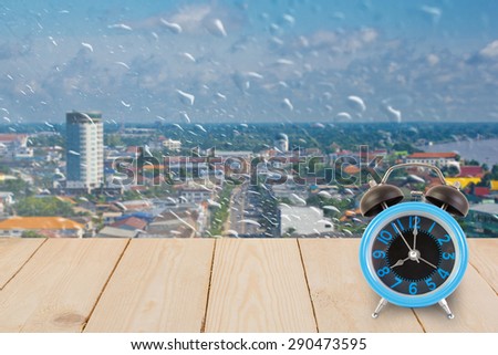 Blue alarm clock on wood texture on rain drops on a window or water drops with cityscape view.