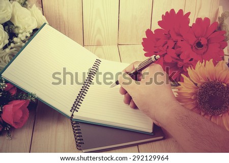 Vintage style - Hand holding a pen with notepad and flower on wood texture.