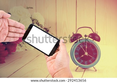 Man hand hold blank touch screen smart phone on vintage wood background and flowers with retro alarm clock.