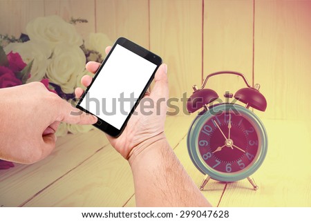 Man hand hold blank touch screen smart phone on vintage wood background and flowers with retro alarm clock.
