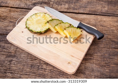 pineapple slice and knife on wooden cutting board, on wooden table top