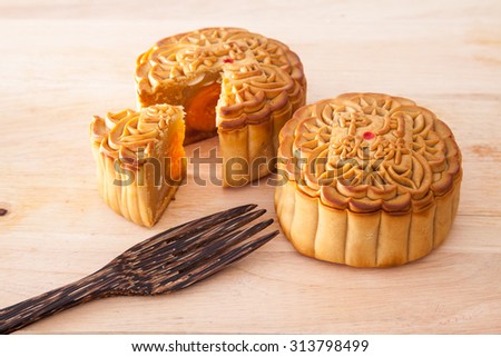Moon cakes for the chinese Mid-Autumn festival with one cut up to show egg yolk and wooden fork, on wooden background