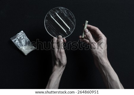 The fight against drugs and drug addiction topic: addict hand holds a mirror with strips of cocaine and drugs around her lie on a dark background, top view in the studio