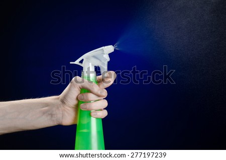 Cleaning the house and cleaner theme: man\'s hand holding a green spray bottle for cleaning on a dark blue background in studio