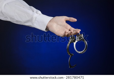 Dishonest and a prison doctor topic: the hand of man in a white shirt with handcuffs on a dark blue background in studio, put handcuffs on the doctor, the illegal sale of organs