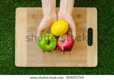 Vegetarians and cooking on the nature of the theme: human hand holding a red, apple green and lemon yellow on the background of a cutting board and green grass top view