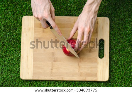 Vegetarians and cooking on the nature of the theme: human hand holding a knife and a red apple on the background of a cutting board and green grass top view