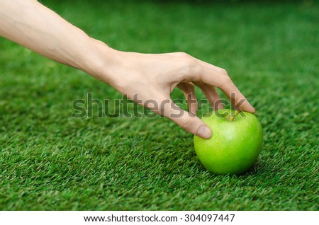 Vegetarians and fresh fruit and vegetables on the nature of the theme: human hand holding a green apple on a background of green grass