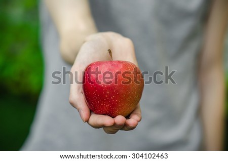 Vegetarians and fresh fruit and vegetables on the nature of the theme: human hand holding a red apple on a background of green grass