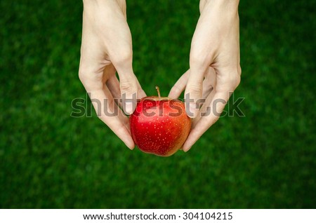 Vegetarians and fresh fruit and vegetables on the nature of the theme: human hand holding a red apple on a background of green grass top view