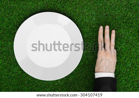 Business lunch and fresh fruit and vegetables on the nature theme: the human hand in black suit shows on the plate on a background of green grass top view