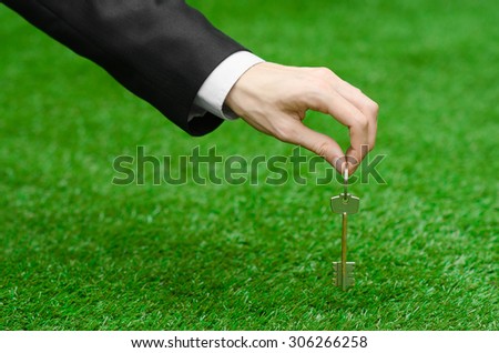 Buying a new house or land and business topic: hand in a black suit holding a key to the new house on the background of green grass