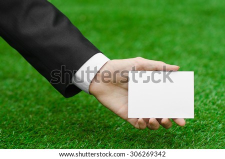 Discounts and business topic: hand in a black suit holding a white blank card on green grass background