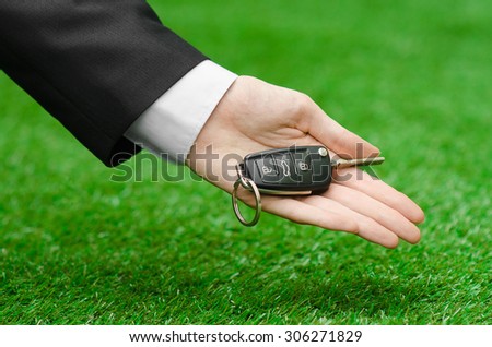 The new machine and a business topic: hand in a black suit holds the keys to the new car on a background of green grass