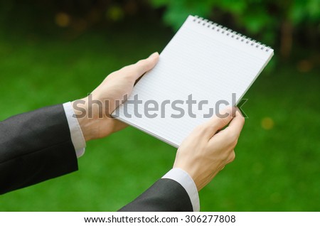 Day of knowledge and business topic: the hand of man in a black suit holding a notebook and pencil top view on a background of green grass