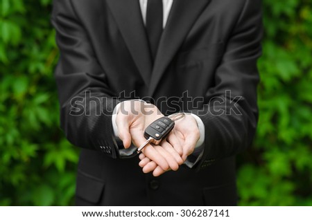 New car and business theme: a man in a black suit holds the keys of a new car on a background of green grass