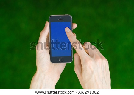 Human hand holding a modern mobile phone with a blue screen on a background of green grass first-person view