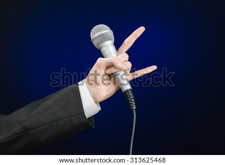 Business and speech topic: Man in black suit holding a microphone on a gray dark blue isolated background in studio