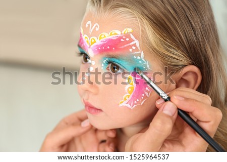 Artist painting face of little girl indoors
