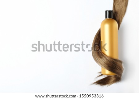 Shampoo bottle wrapped in lock of hair isolated on white, top view. Natural cosmetic products